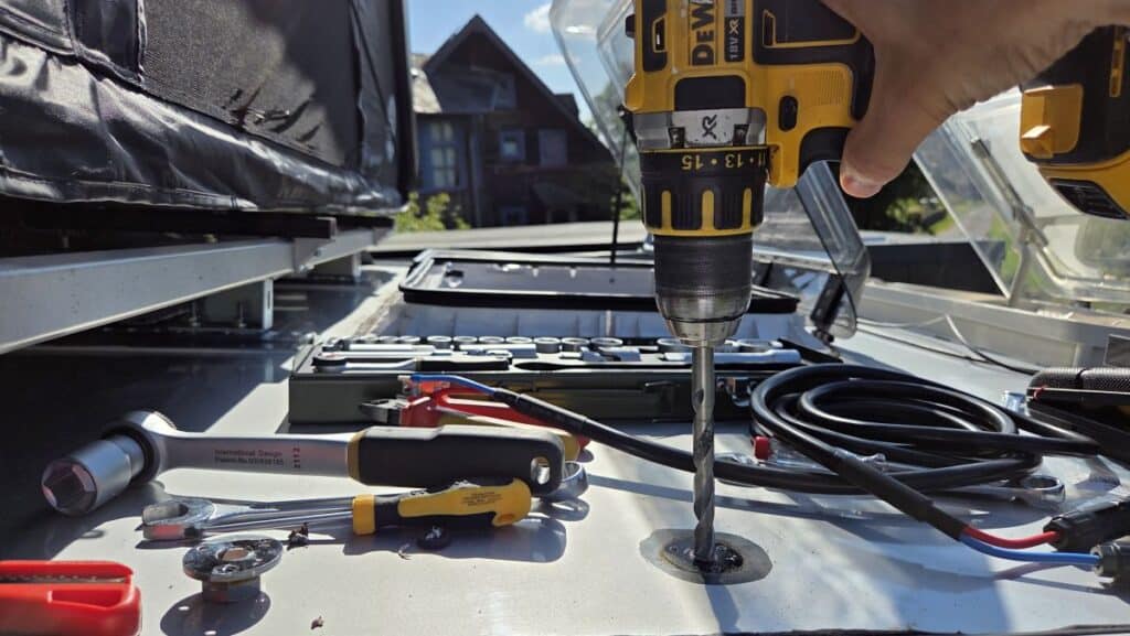 Aufweiten des Lochs für die neue Dachdurchführung mit dem Akkubohrer, daneben das neue Solarkabel und Werkzeug